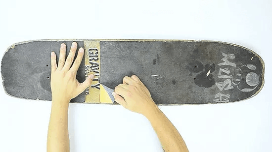A person cutting a skateboard in half with a pair of scissors.