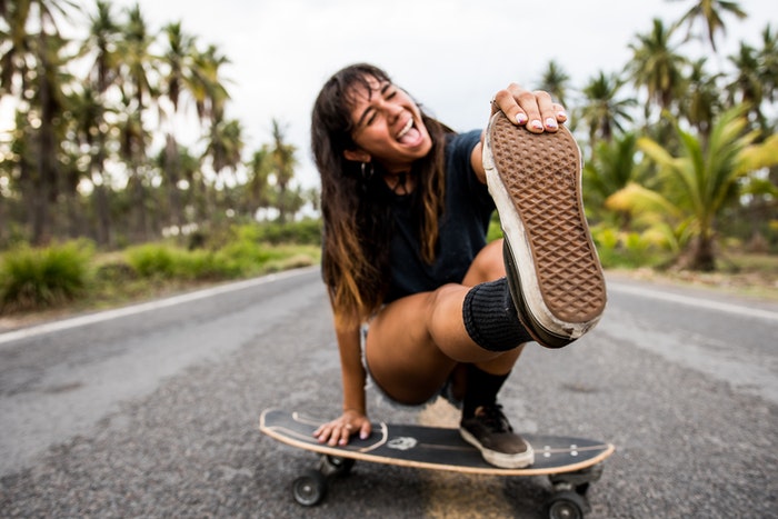 A woman skateboarding on a road with palm trees. (skateboard, palm trees)