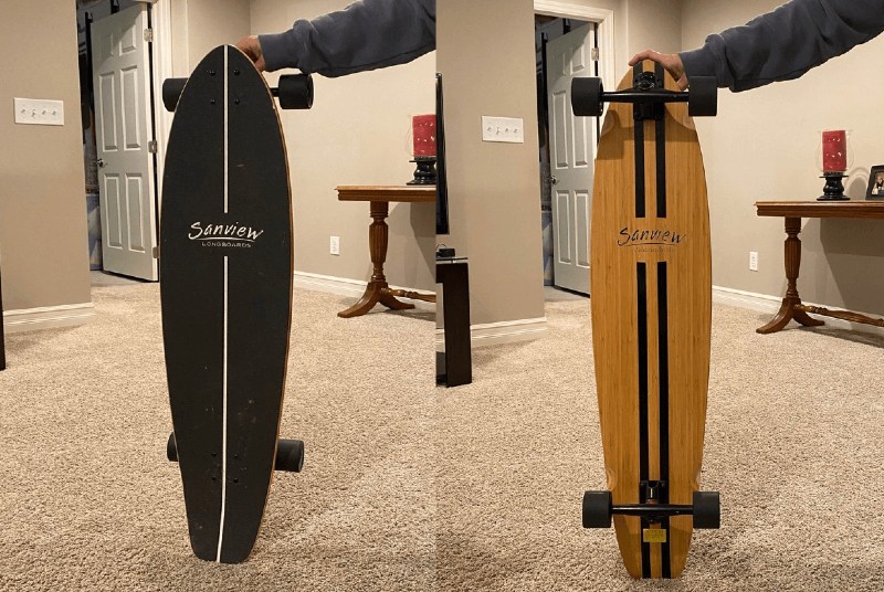 A person is holding a wooden skateboard in a living room.